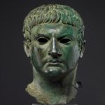 Древнеримская античная скульптура — погрудный портрет мужчины из сильно окисленной зеленой бронзы. Поверхность металла покрыта неоднородной, толстой и бугристой патиной ярко-зеленых и бирюзовых тонов, скрывающей металлический блеск.